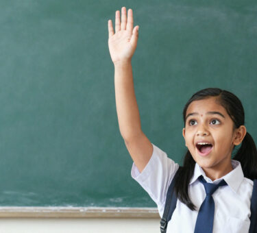 Young Indian girl in school uniform raising hand eagerly asking question, bright curious expression,