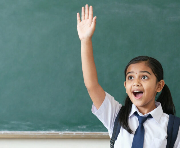 Young Indian girl in school uniform raising hand eagerly asking question, bright curious expression,